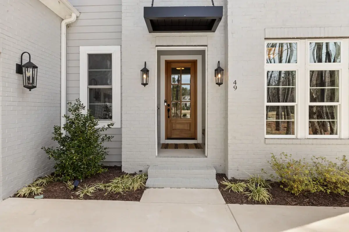 Wooden front door framed by white brick, sidelights and green plants.