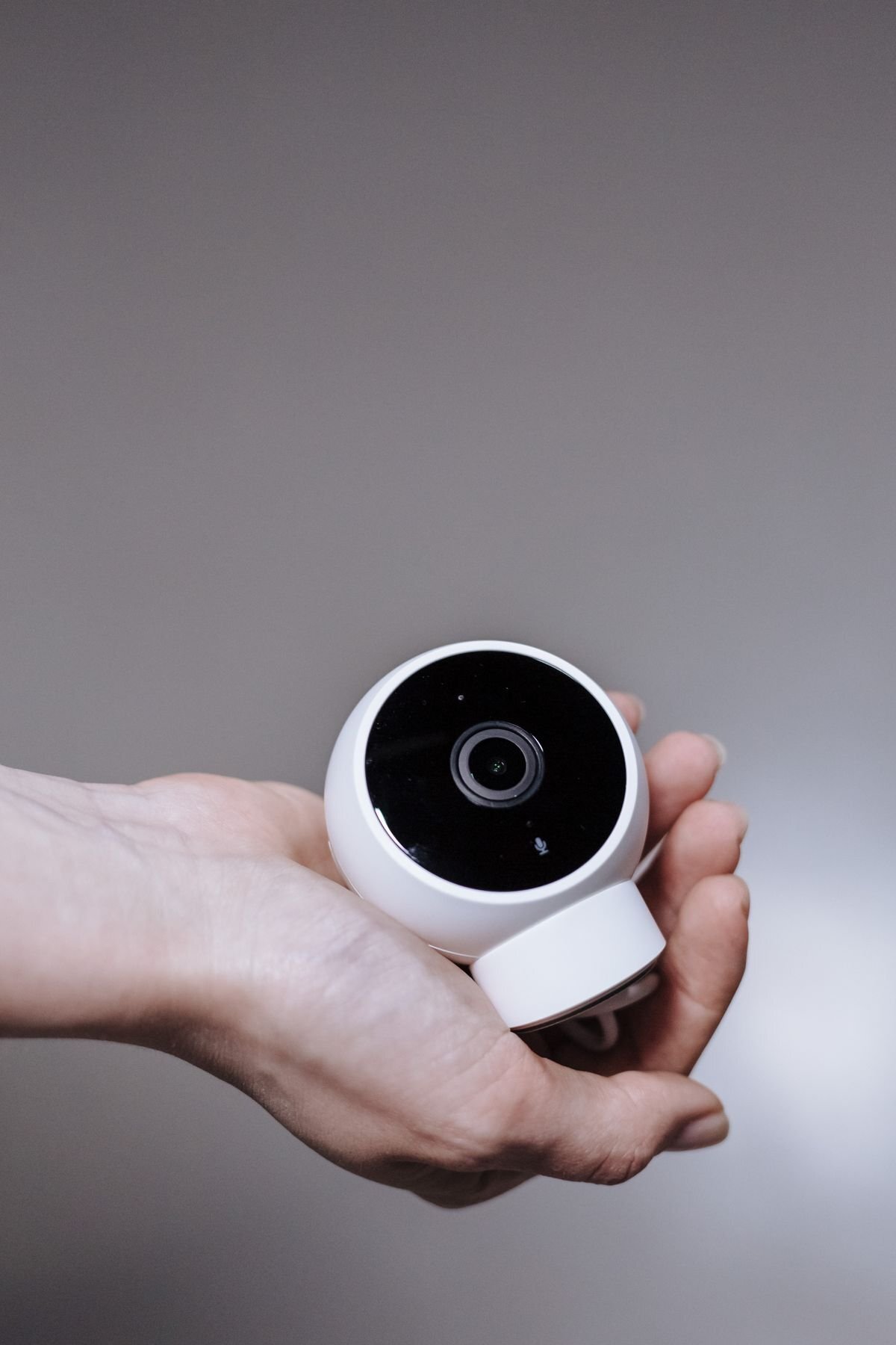 Hand holding a small white indoor security camera